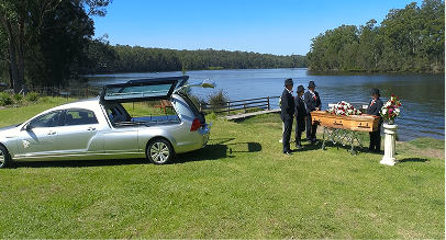 hearse by the riverside with funeral directors standing around a coffin