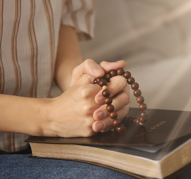 close-up of folded hands holding a rosary
