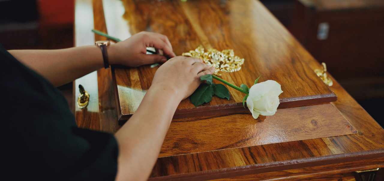 hands placing a single white rose on a casket